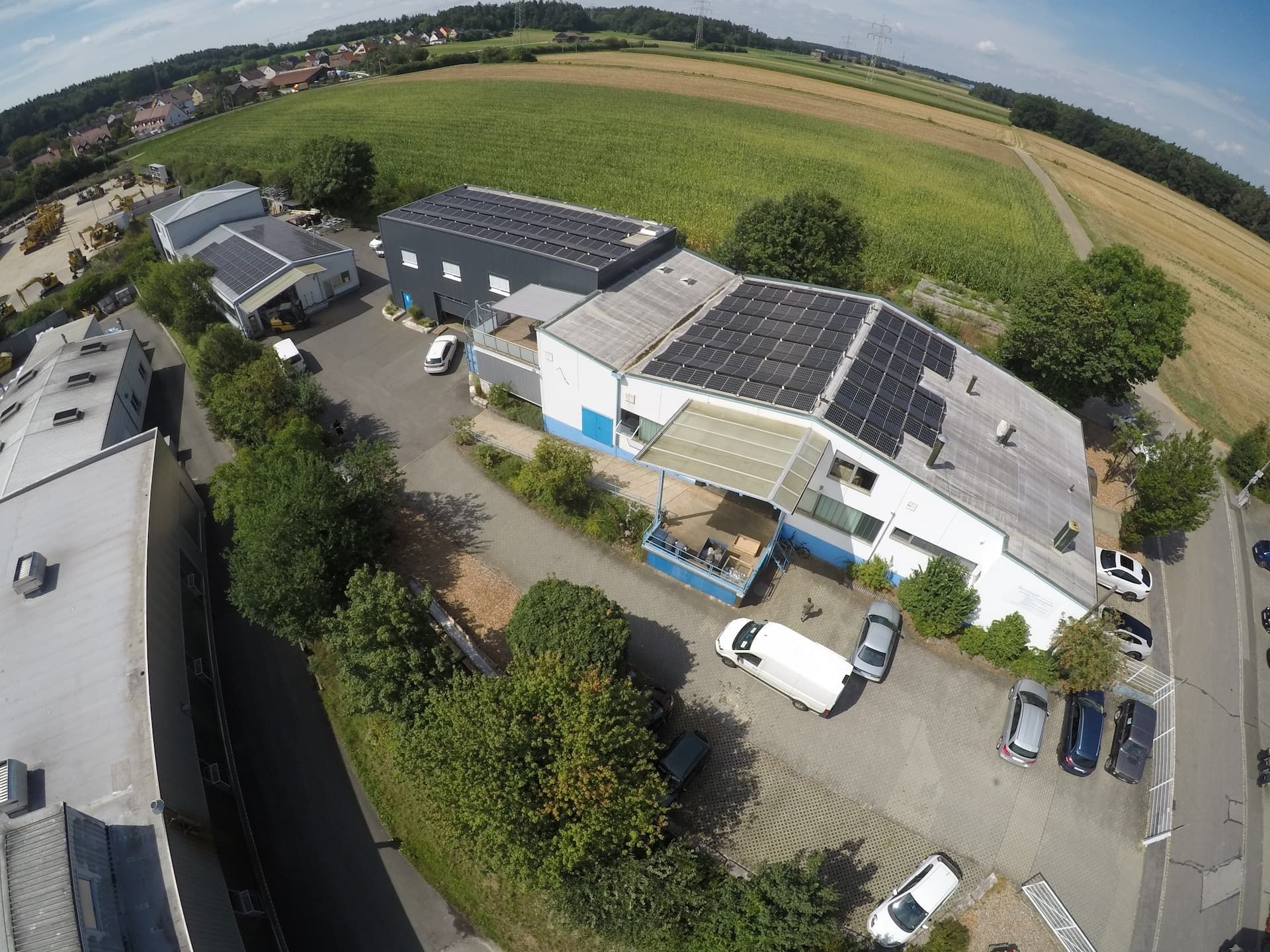 Luftaufnahme eines Industriebetriebs mit Solaranlagen und Parkplatz in ländlicher UmgebungLuftaufnahme eines Industriebetriebs mit Solaranlagen und Parkplatz in ländlicher Umgebung